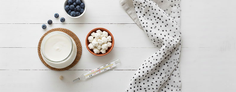 Bodegón minimalista que representa la temperatura ideal de fermentación: un frasco de kéfir de leche en un ambiente cálido y luminoso, junto a un termómetro analógico de madera y un paño de lino, sugiriendo un control ambiental óptimo entre 20°C y 22°C