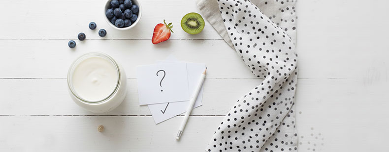 Composición limpia y minimalista para la sección de preguntas frecuentes: un frasco de cristal con kéfir de leche recién hecho, una cuchara de madera con nódulos frescos y elementos naturales sobre un fondo blanco luminoso