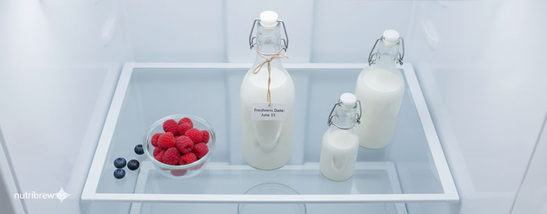 Interior de un refrigerador moderno con botellas de cristal llenas de kéfir de leche fermentado, organizadas para mantener la frescura y las propiedades probióticas del producto terminado de Nutribrew.