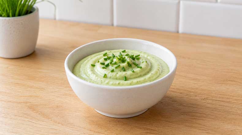 Cuenco blanco con crema espesa de kéfir y aguacate verde decorada con cebollino fresco picado encima