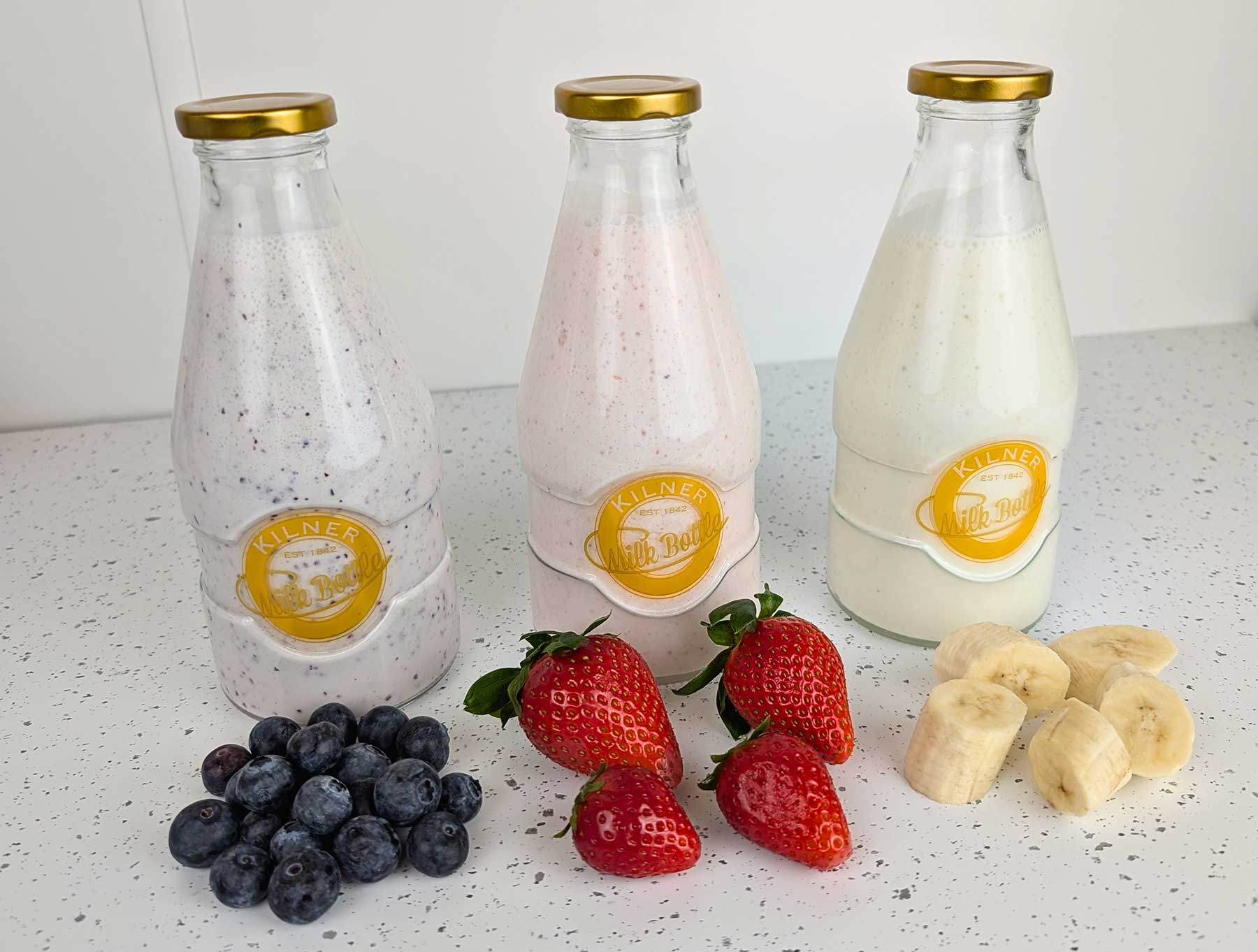 Botellas de kéfir de leche con sabores de arándanos, fresa y plátano sobre encimera blanca